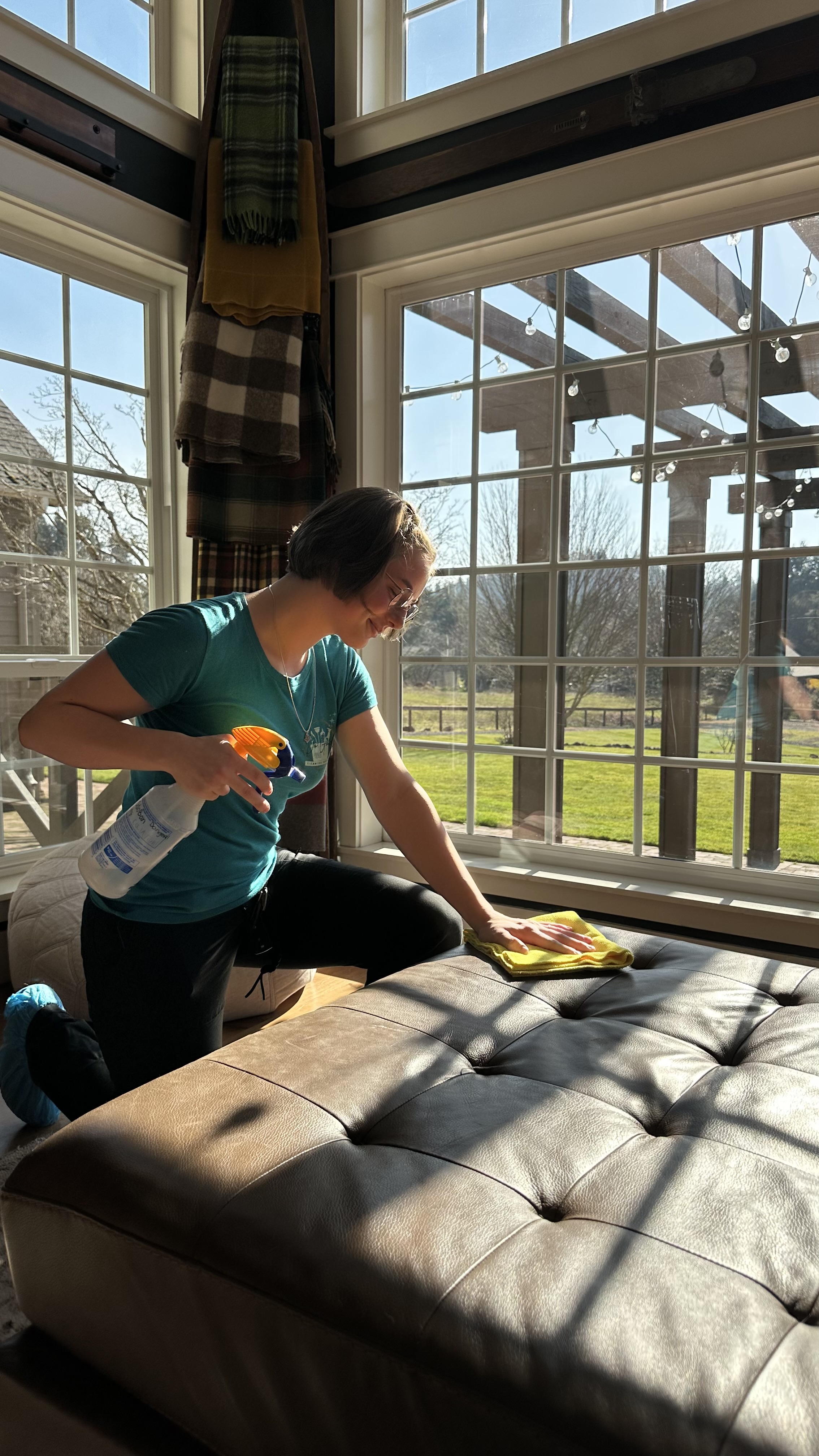 A Do Good Cleaning Services team member cleaning an ottoman beside a sunny window